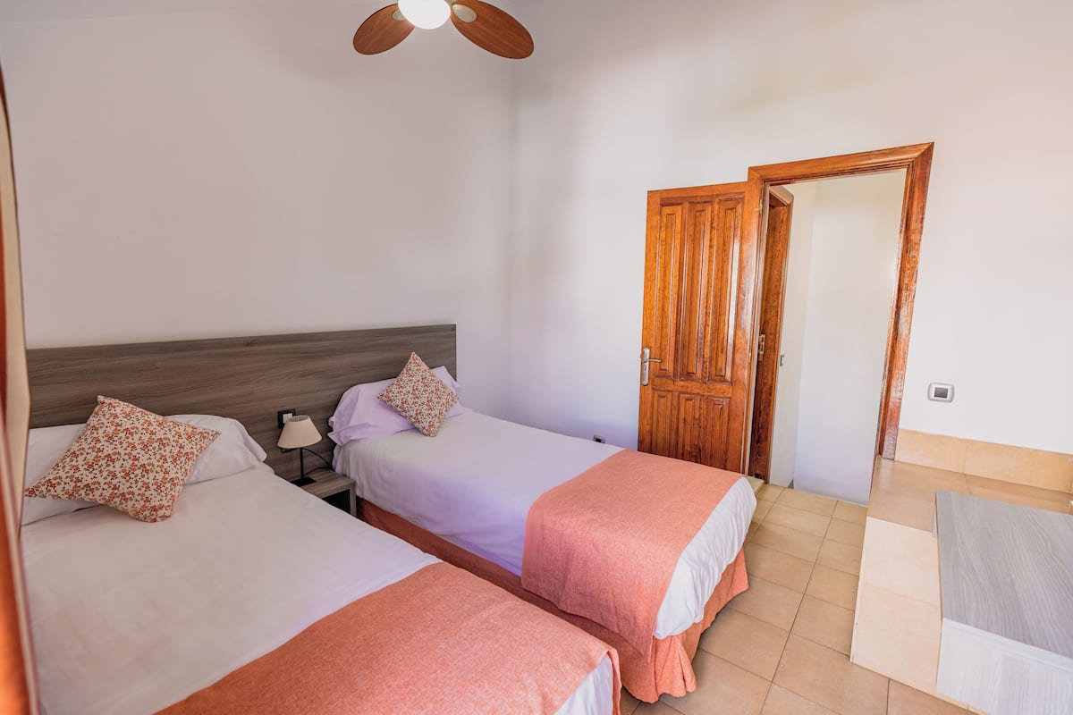 Una habitación de hotel con dos camas, una puerta de madera y un ventilador de techo.