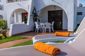 Un espace extérieur ensoleillé, aménagé avec des sièges et comprenant une chaise longue et une serviette enroulée.