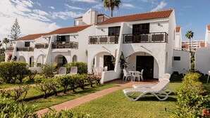 Un bâtiment blanc avec des toits recouverts de tuiles rouges, de nombreux balcons et un jardin agrémenté de chaises longues blanches.