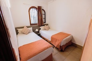 Een kamer met twee bedden, een raam met gordijnen, een nachtkastje en een spiegel.
