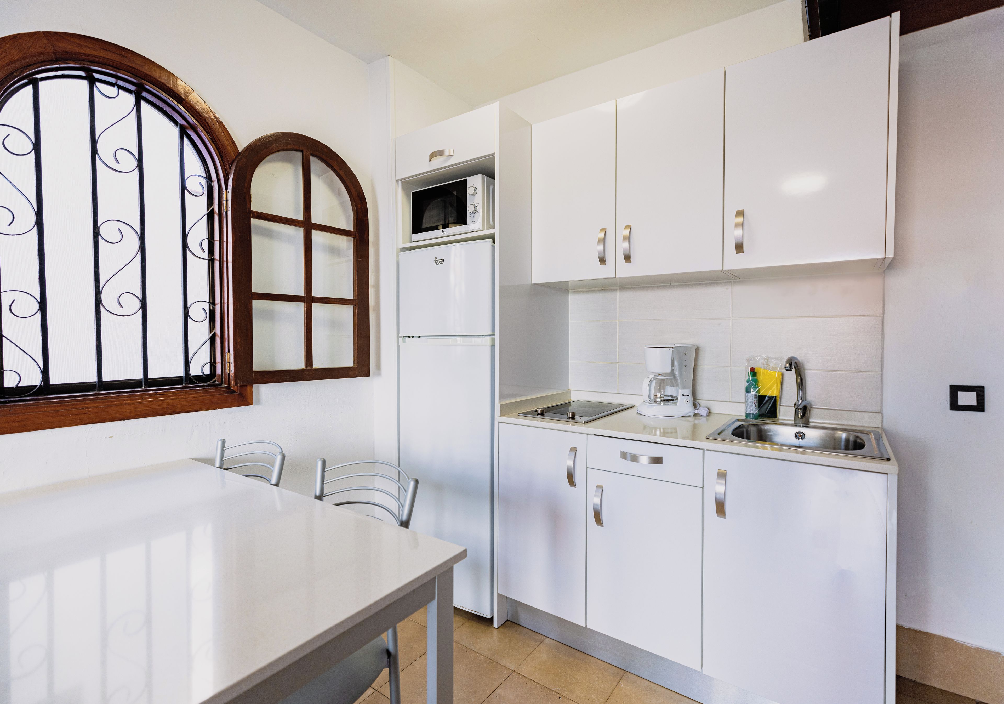 A compact kitchen with white cabinets, a microwave, a refrigerator, and a sink.