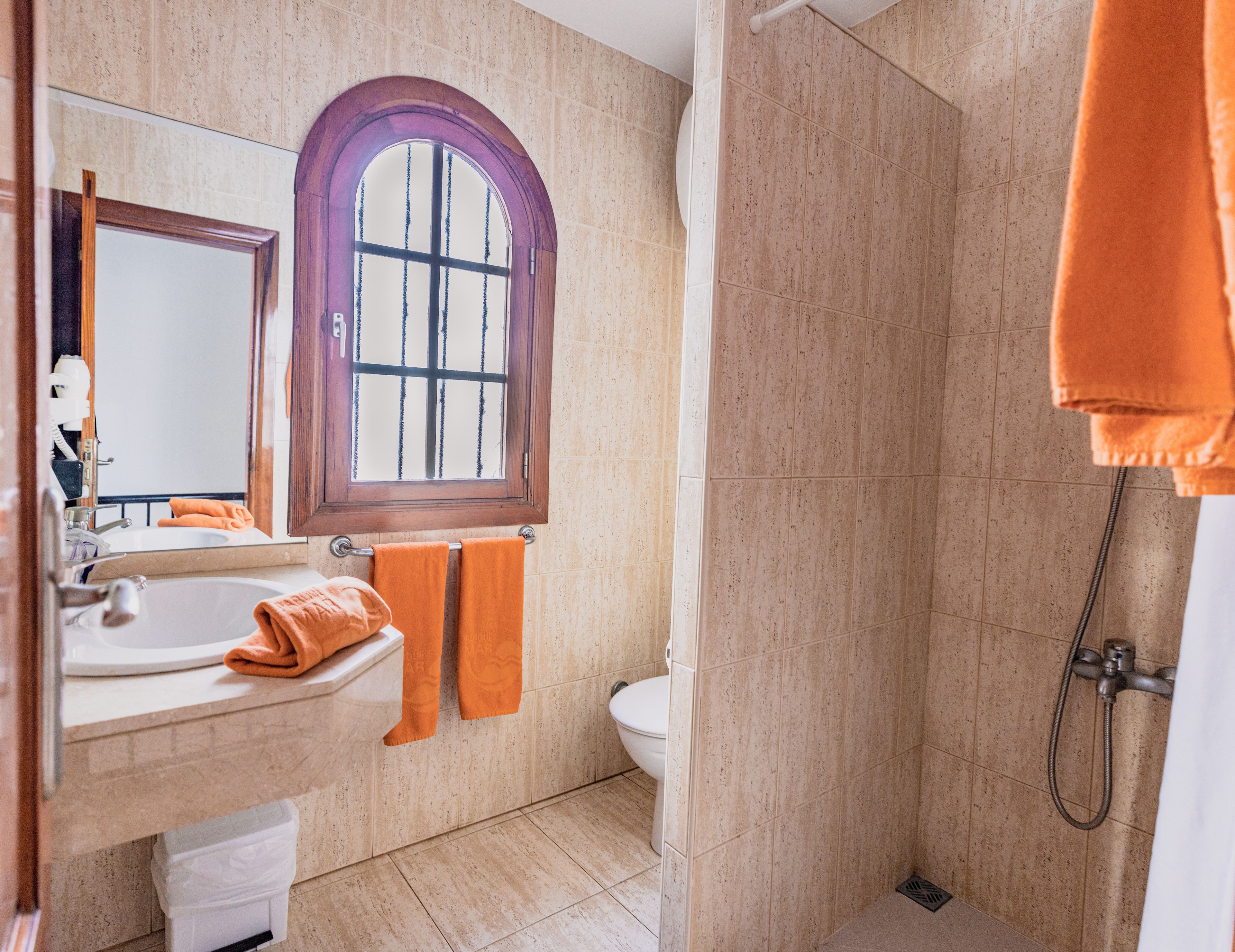 Een badkamer met een wastafel, spiegel, raam en douche.