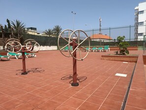 Outdoor exercise equipment, a fenced area, and a building in the background. - Parquemar (San Bartolomé de Tirajana)