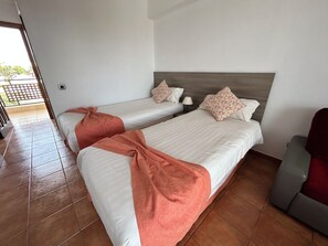 A hotel room with two single beds, a wooden headboard, a red chair, and a tiled floor. - Parquemar (San Bartolomé de Tirajana)