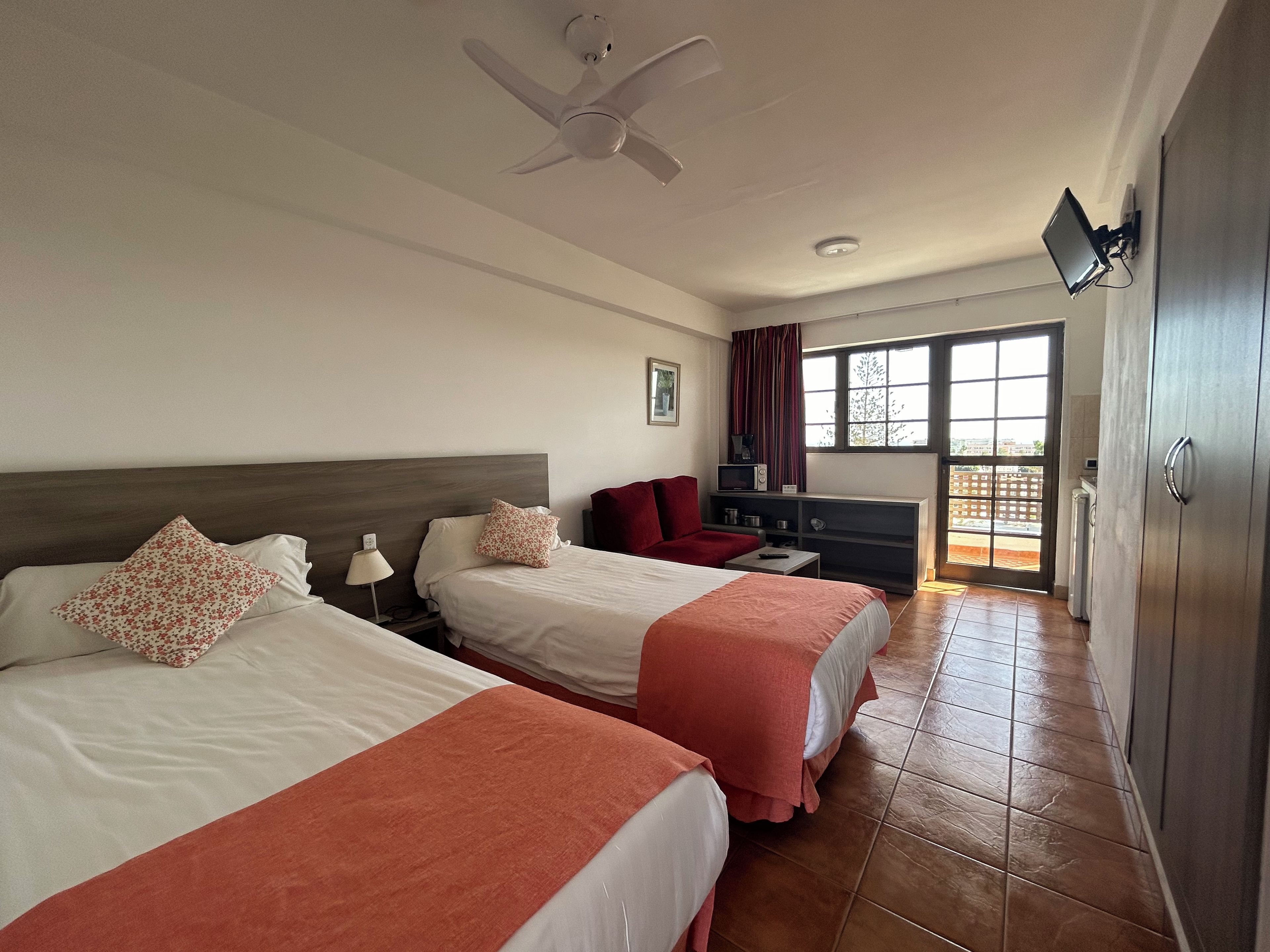 Habitación de hotel con dos camas, un escritorio, un televisor y vistas por una ventana grande.