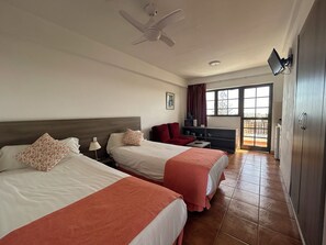 Une chambre d’hôtel avec deux lits, un bureau, une télévision et une vue sur l’extérieur grâce à une grande fenêtre.