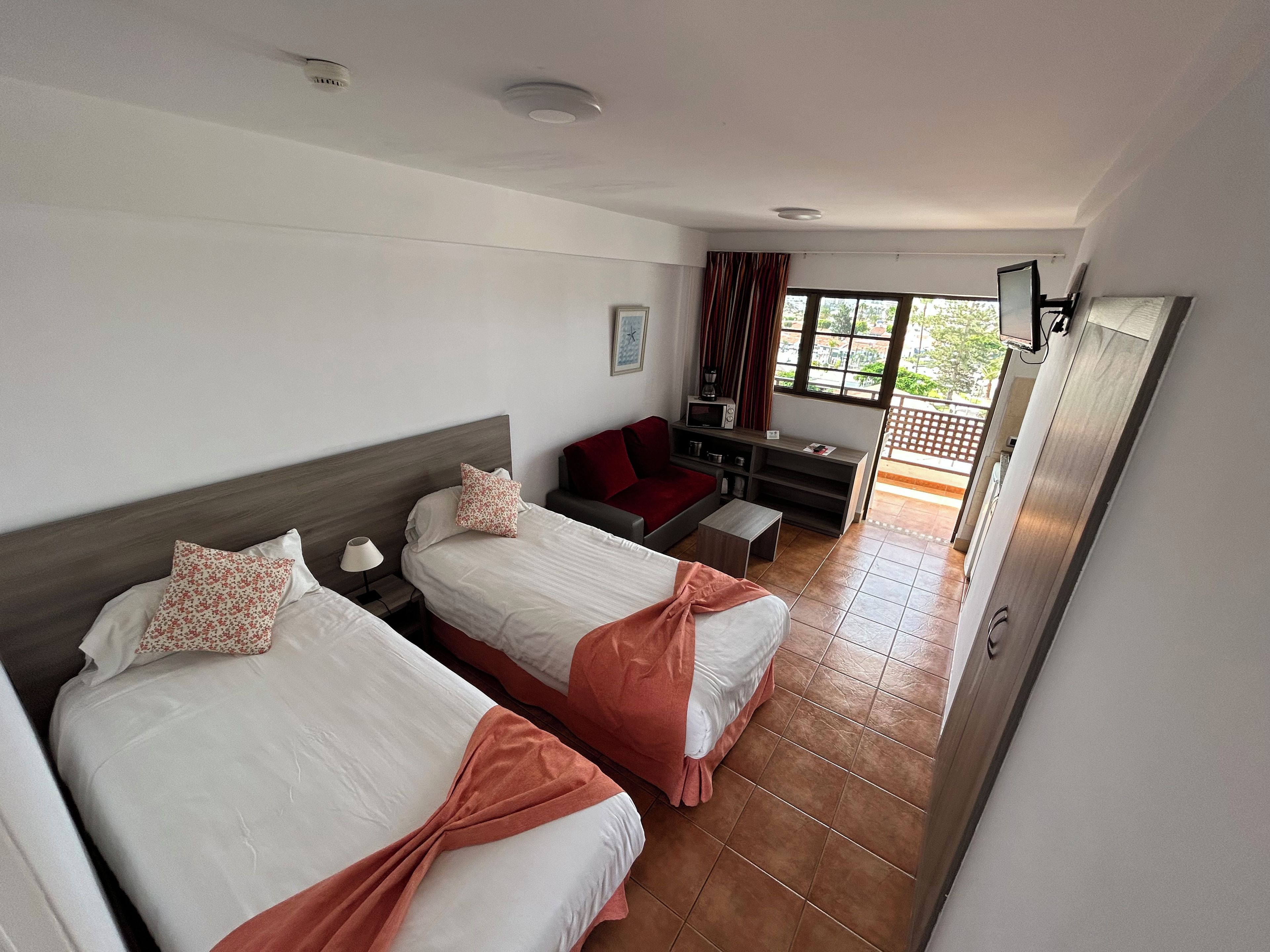 Habitación de hotel con dos camas, un sofá, una mesita y un televisor.