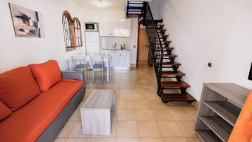 A modern living room with a sofa, a coffee table, and a staircase leading to a kitchen area.