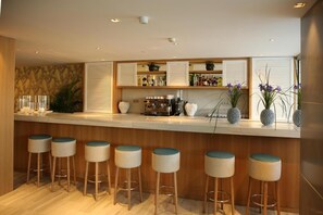 A modern bar area with a wooden counter, bar stools, and a variety of bottles and decorative items.