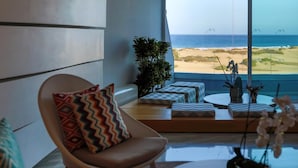 A modern living room with a view of the beach, a comfortable chair, a round table, and a potted plant. - Santa Mónica Suites Hotel (San Bartolome de Tirajana)