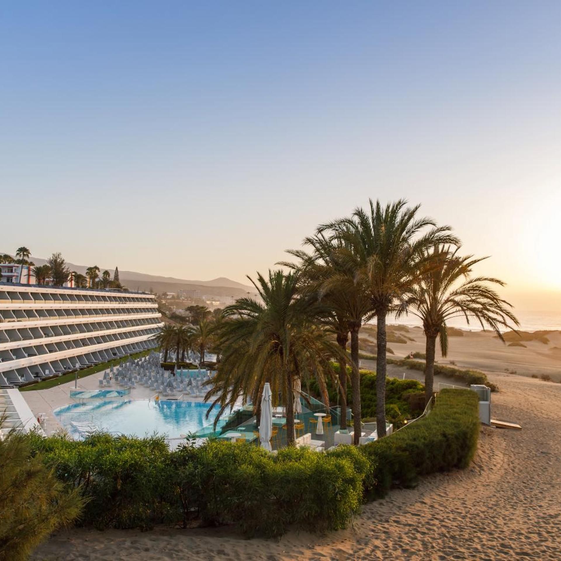 A resort with a swimming pool, palm trees, and a desert landscape in the background.