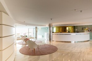 A modern hotel lobby with a reception desk, seating area, and a view of the outdoors.