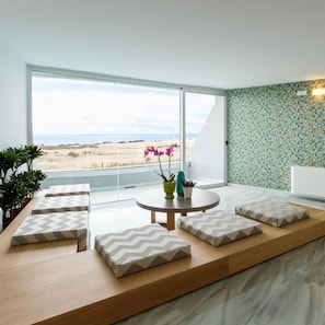 A modern living room with a large window, a round table, and a seating area with patterned cushions. - Santa Mónica Suites Hotel (San Bartolome de Tirajana)