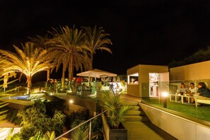 A nighttime outdoor area with palm trees, a pool, and a seating area with umbrellas. - Santa Mónica Suites Hotel (San Bartolome de Tirajana)