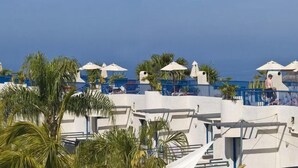 Un hôtel situé sur la côte, avec des bâtiments blancs, des palmiers et un ciel d’un bleu limpide.