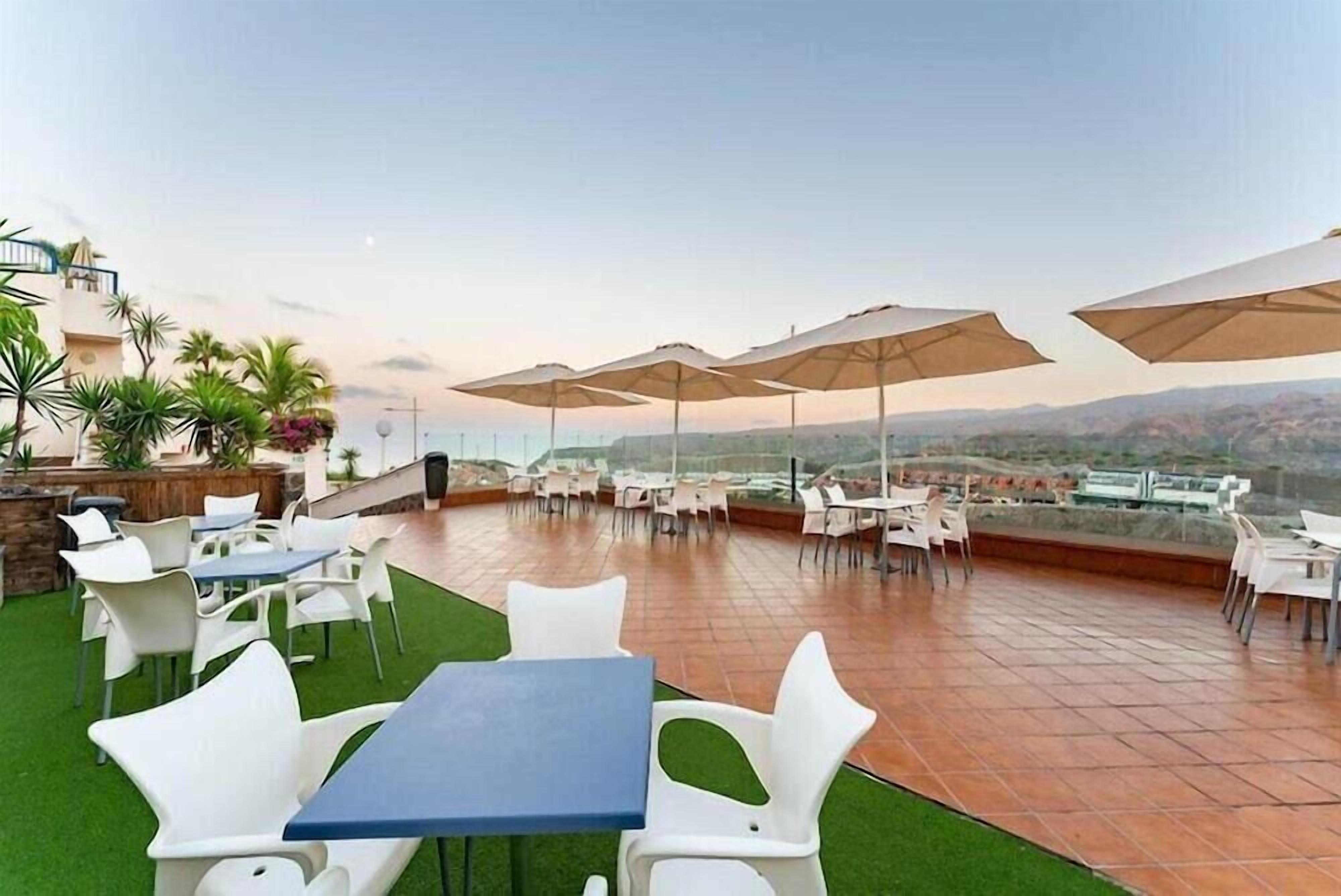 An outdoor terrace with tables and chairs, umbrellas, and a view of the landscape.