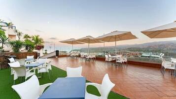 An outdoor terrace with tables and chairs, umbrellas, and a view of the landscape.