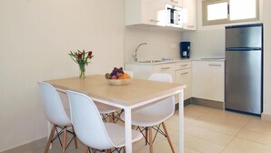 Une cuisine compacte avec des meubles blancs, un réfrigérateur en acier inoxydable et un coin repas comprenant une table en bois et des chaises blanches.
