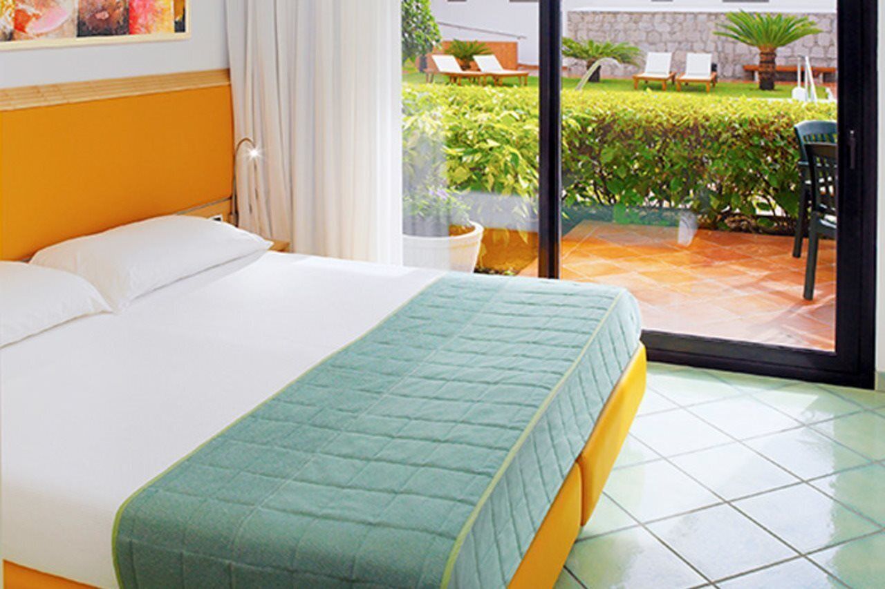 Een hotelkamer met een bed, uitzicht op het terras en een raam met gordijnen.