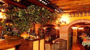 A rustic interior with stone walls, wooden beams, and a bar area with a plant-covered wall. - El Greco (Mogan)