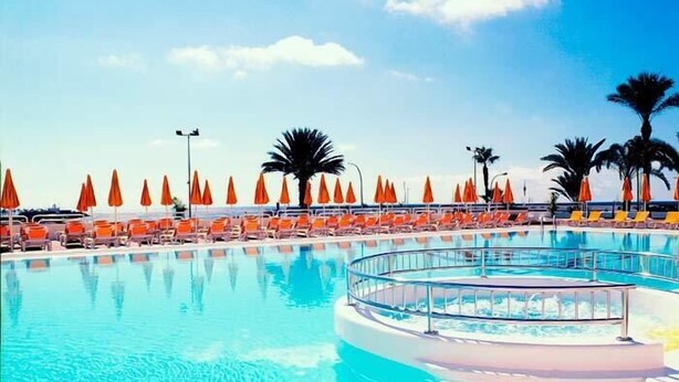 A pool area with lounge chairs and umbrellas, surrounded by palm trees. - El Greco (Mogan)