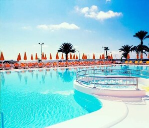 Un espace piscine agrémenté de chaises longues et de parasols, entouré de palmiers.
