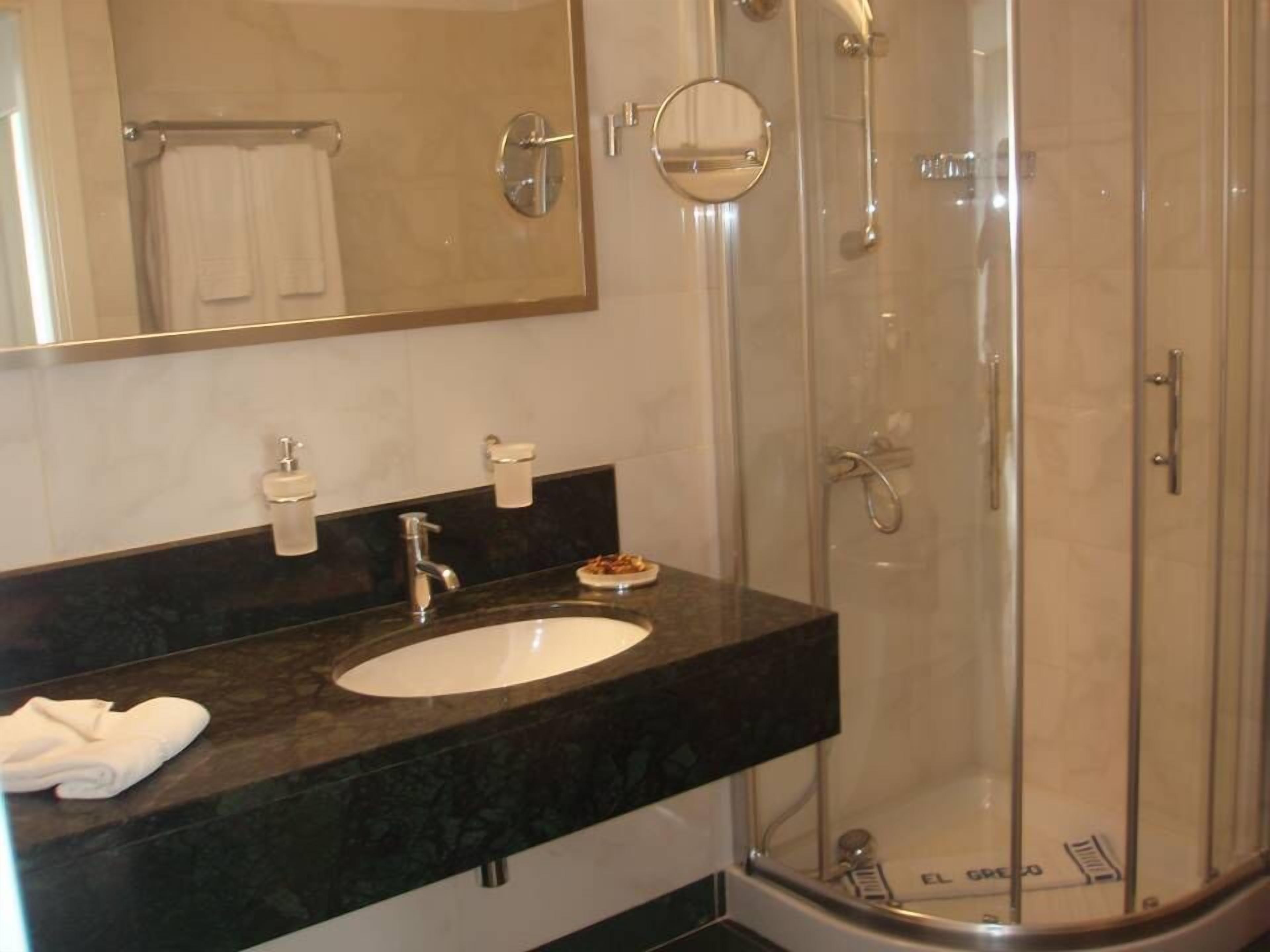 A modern bathroom with a marble countertop, a white sink, a glass shower enclosure, and a large mirror.