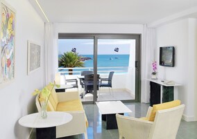 Habitación de hotel con balcón, sofá, mesa de centro, televisión y obras de arte en las paredes.