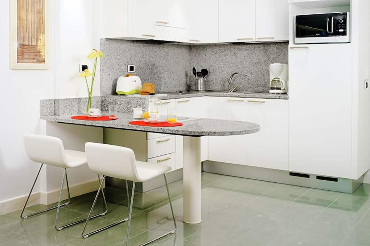 Cozinha moderna com armários brancos, bancada de granito e micro-ondas embutido. Há duas cadeiras brancas na ilha, e um vaso com flores na bancada.