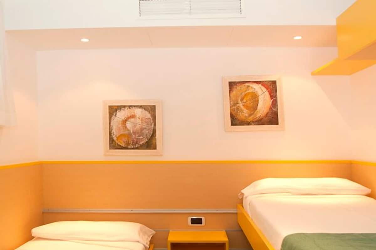 Quarto de hotel com duas camas, uma pequena mesa de cabeceira e duas pinturas penduradas na parede.
