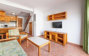 A compact living space with a kitchenette, a dining area, a sofa, a TV, and a staircase. - Montecarlo (Mogan)
