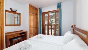 Une chambre d’hôtel avec un lit, un bureau en bois, un miroir et un balcon donnant sur des immeubles.