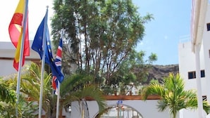 Une entrée d’immeuble avec des marches menant à un portail, le tout entouré de palmiers et de drapeaux.