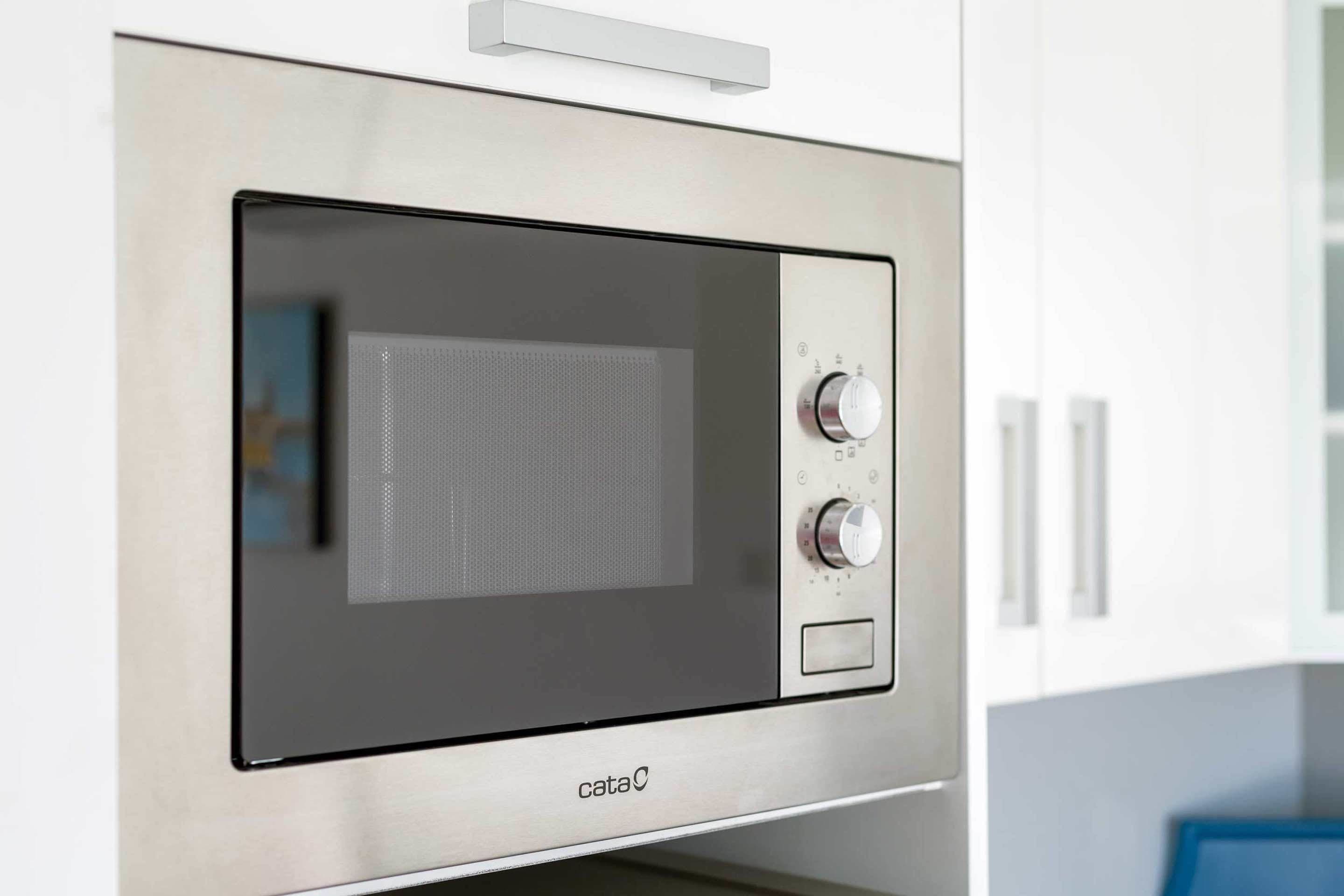 Et moderne køkken med en indbygget mikrobølgeovn i rustfrit stål, et kontrolpanel med drejeknapper og et digitalt display.