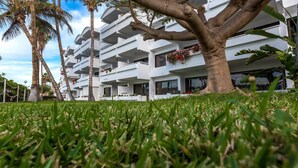 Un hôtel moderne à plusieurs étages, doté de balcons, entouré de palmiers et bordé de pelouses bien entretenues.