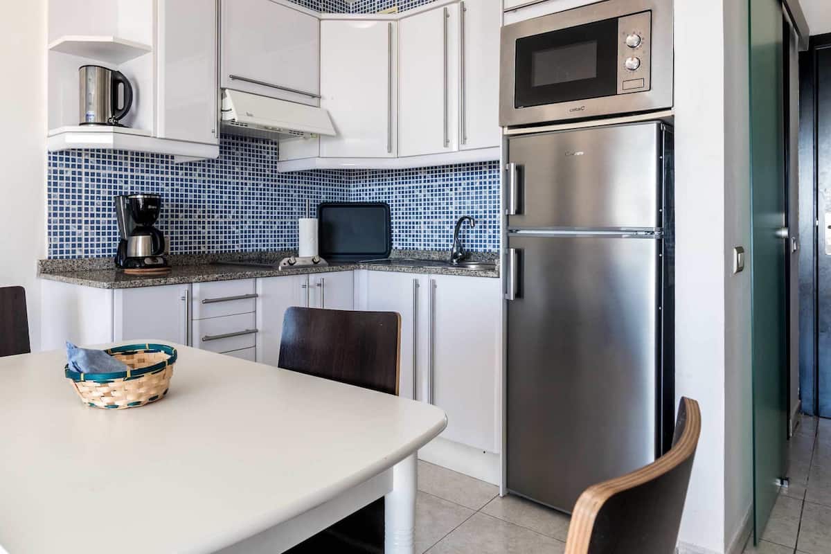 A compact kitchen with white cabinets, a stainless steel refrigerator, a microwave, and a coffee maker.