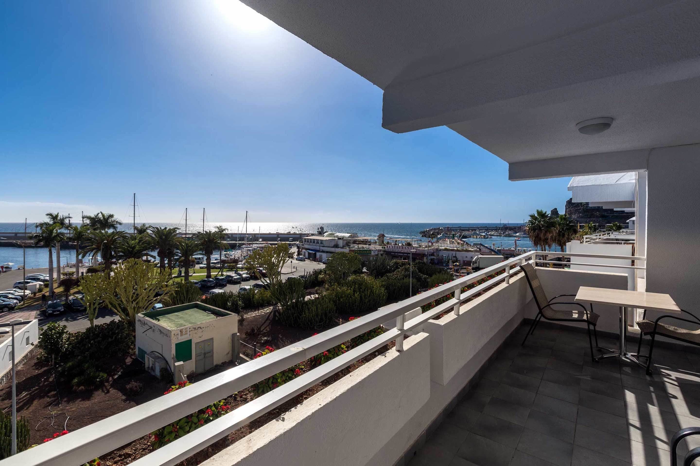 Un balcon offrant une vue sur un port de plaisance, des palmiers et un ciel dégagé.
