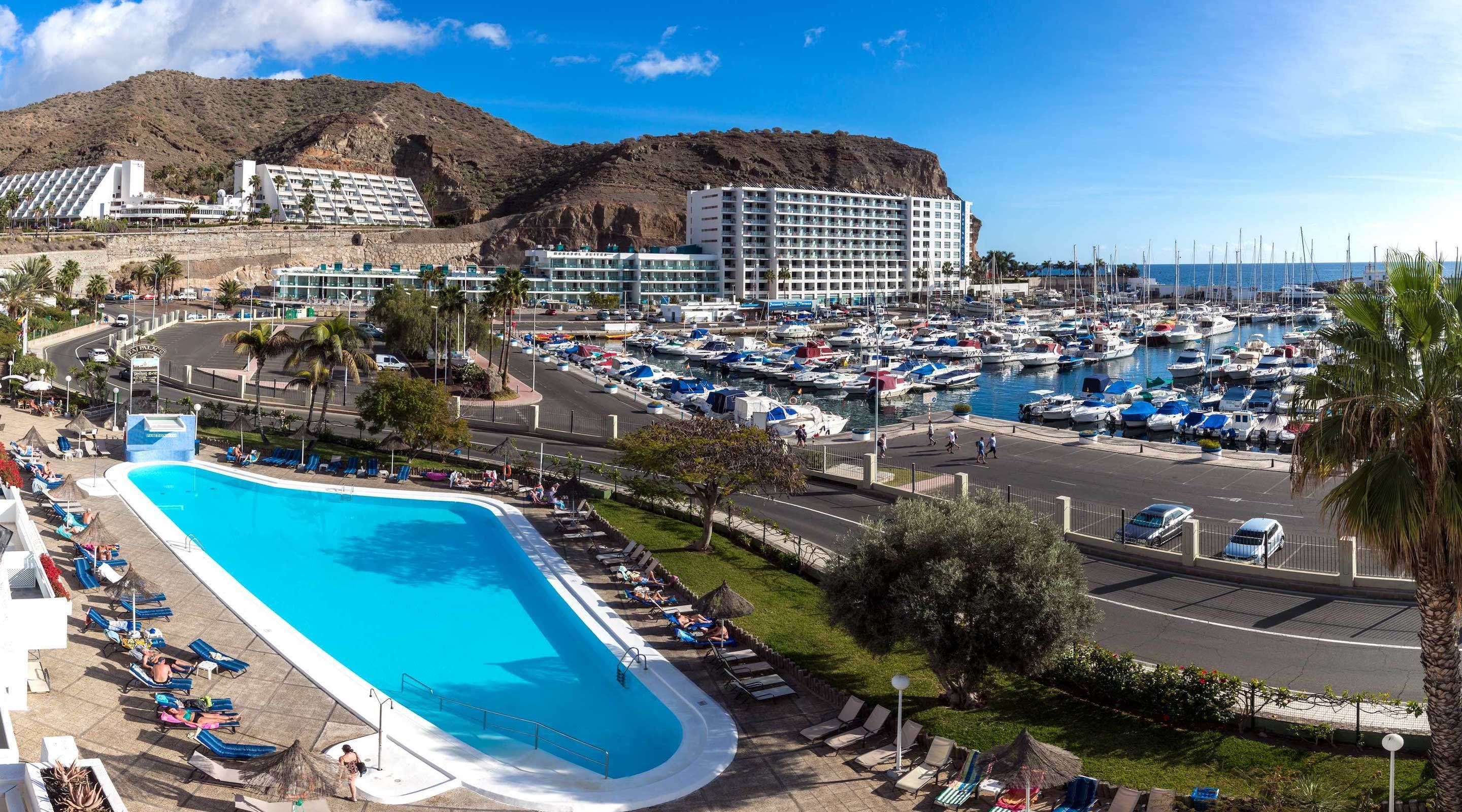 Un resort con una grande piscina, un porto turistico con numerose imbarcazioni e una montagna sullo sfondo.