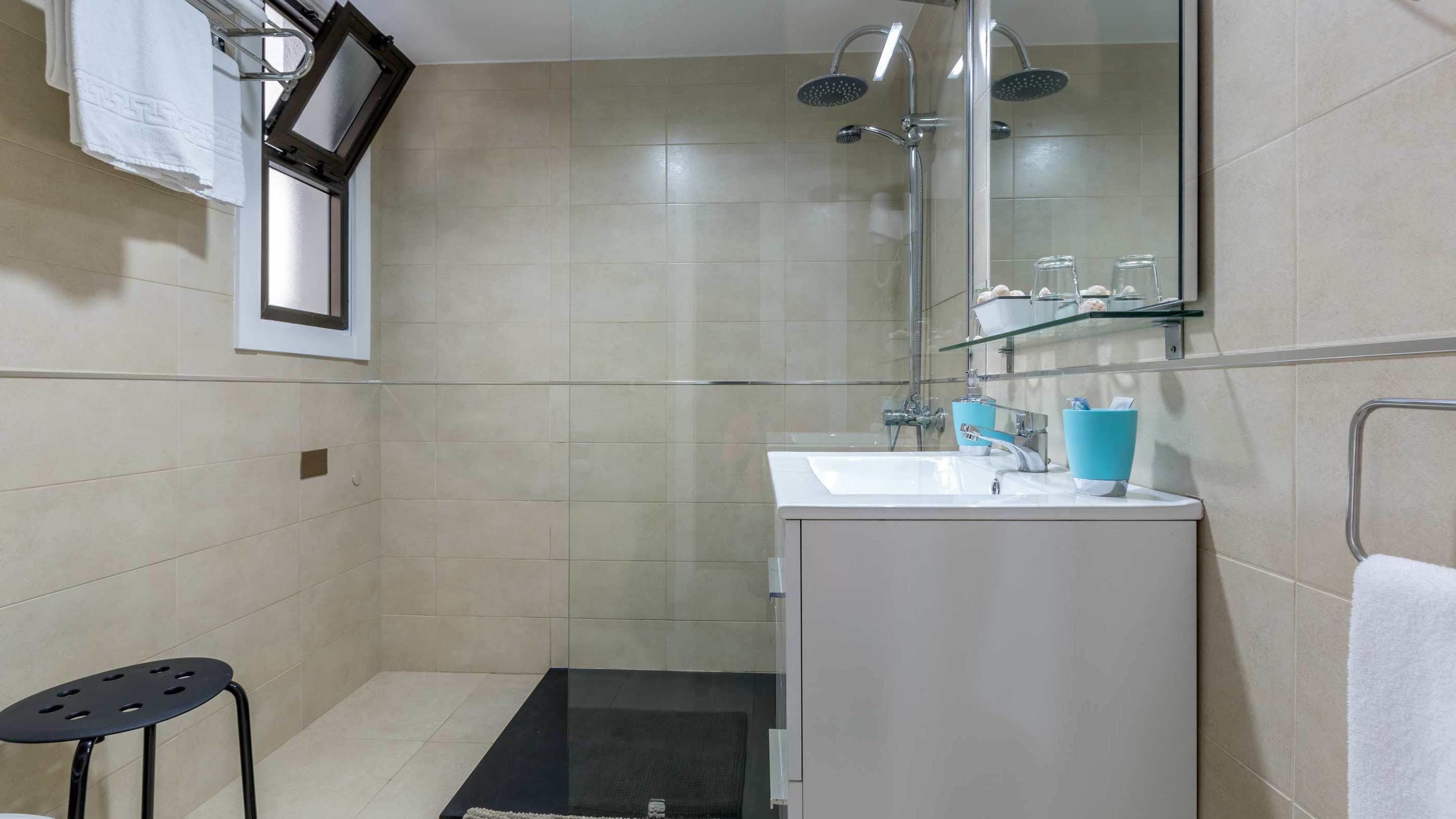 A modern bathroom with a glass shower enclosure, a white sink with blue fixtures, and a black mat on the floor.