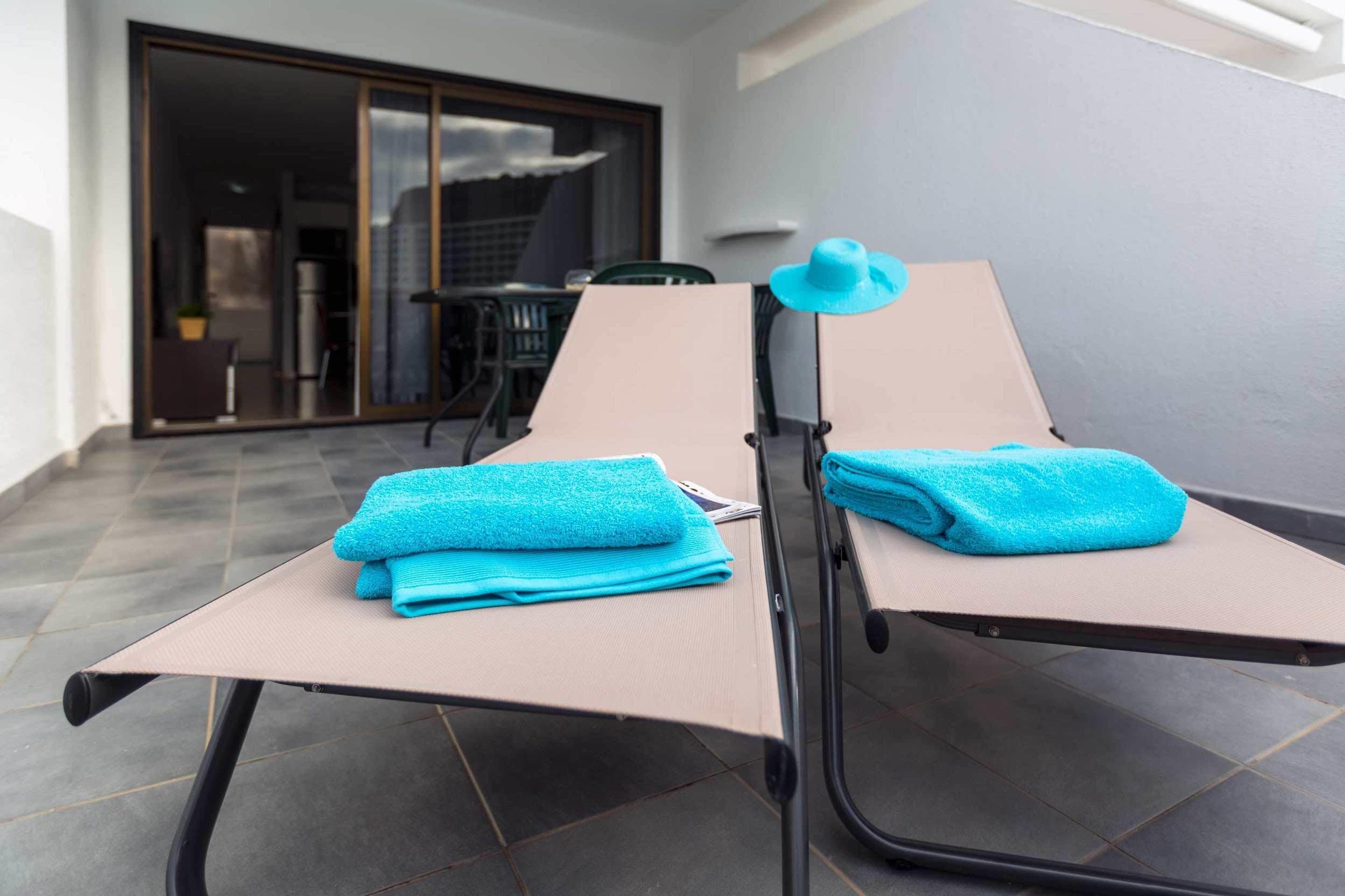 A sun lounger with a blue towel and a hat, and a sliding glass door leading to an outdoor area.