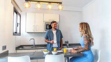Una cocina moderna con armarios blancos, un lavamanos de acero inoxidable y un microondas empotrado.