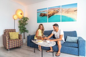 Una sala moderna con un sofá azul, un sillón estampado, una mesita redonda y una planta en maceta.