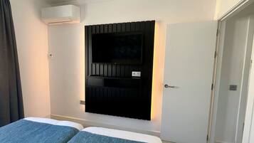 A hotel room with a bed, a TV mounted on the wall, and an air conditioning unit.