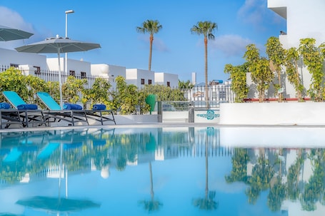 Una piscina al aire libre, sombrillas, sillones reclinables de piscina