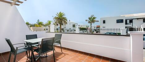 A terrace with a table and chairs, a white wall, and a view of palm trees and buildings.