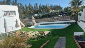 A backyard with a swimming pool, artificial grass, lounge chairs, and a wooden deck. - Apartamentos Miami Playa (San Agustän)