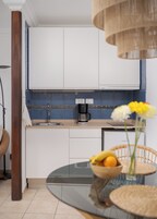 Una cucina moderna con mobili bianchi, una macchina da caffè e un'area pranzo con tavolo in vetro e sedie in vimini.
