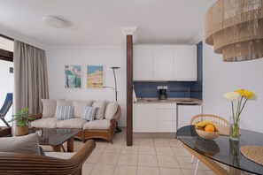 Ein modernes Wohnzimmer mit Sofa, Esstisch und Küchenzeile mit Schränken und einer Kaffeemaschine.