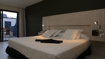 Ein modernes Hotelzimmer mit einem großen Bett, einem Nachttisch mit Lampe und Blick auf den Balkon.