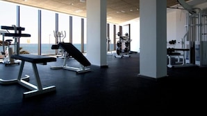 Une salle de sport équipée de divers appareils d’exercice, dotée de grandes fenêtres et offrant une vue sur la mer.